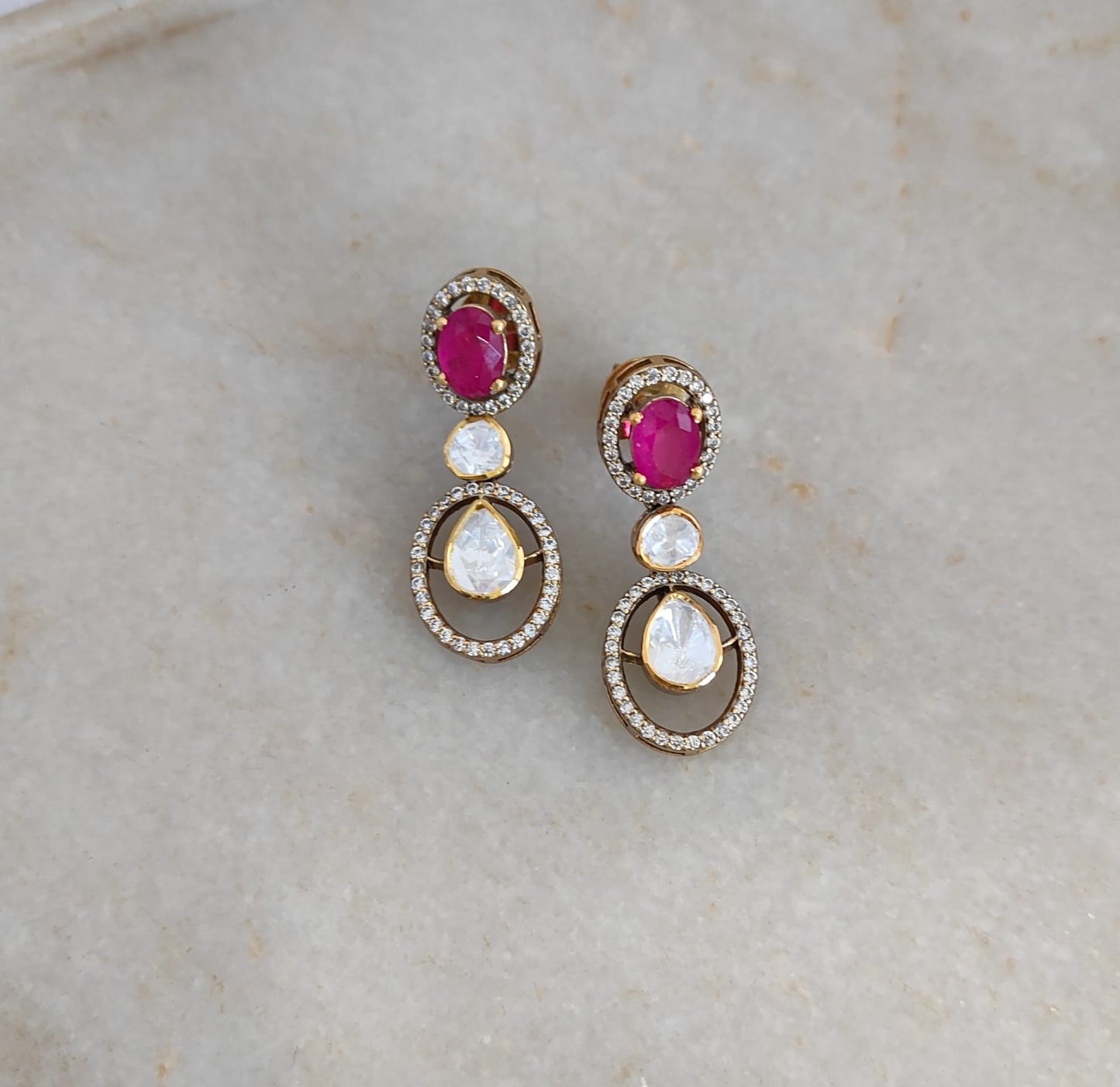 "Ruby Halo drop earrings handcrafted by Arka Jaipur featuring oval ruby color stone, pear-shaped Moissanite Polki stones and cubic zirconia in gold-plated setting"