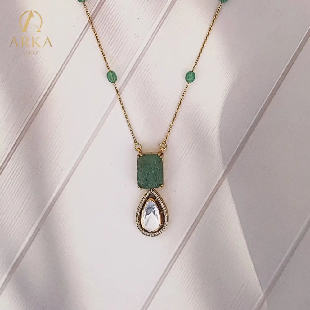 "Elysian Emerald Drops Pendant Handcrafted by Arka Jaipur with carved green gemstone top and teardrop Polki stone drop, outlined with CZ stones, displayed on a wooden background"