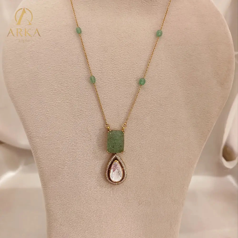 "Elysian Emerald Drop Pendant Handcrafted by Arka Jaipur with carved green gemstone top and teardrop Polki stone drop, outlined with CZ stones, displayed on a wooden background"