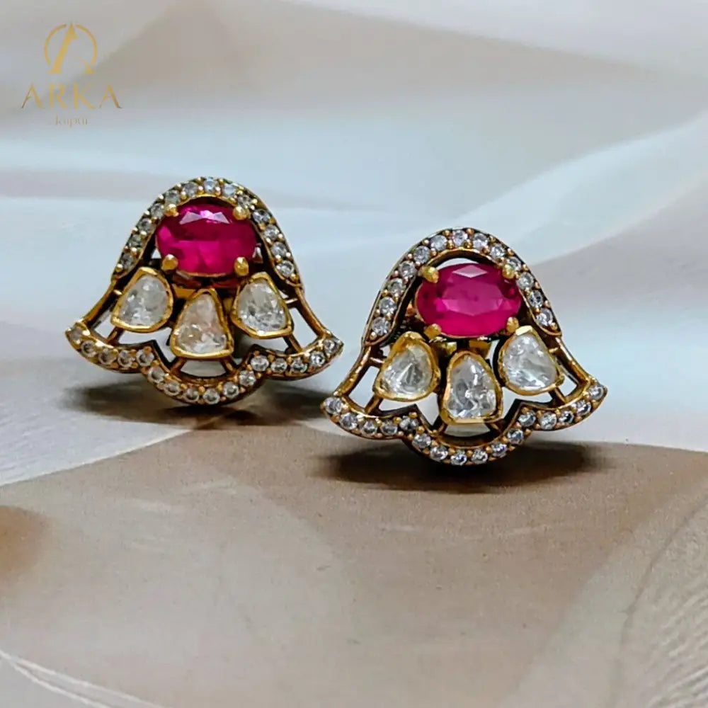 “Scarlet Mist earrings by Arka Jaipur – modern chic designer stud earrings with oval ruby centerpiece, teardrop white stones, gold finish, and diamond outline.”