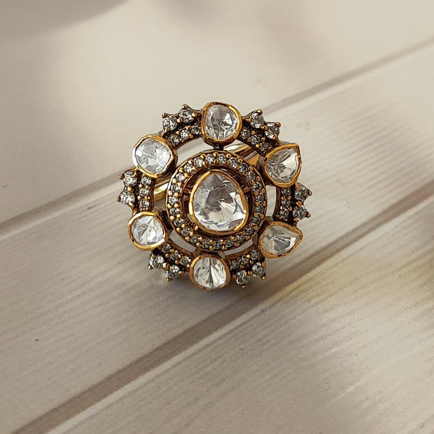 “Eternal Blossom Ring by Arka Jaipur featuring uncut Polki stones, teardrop centre, crystal halo, and gold-tone floral design photographed on a beige wooden background.”