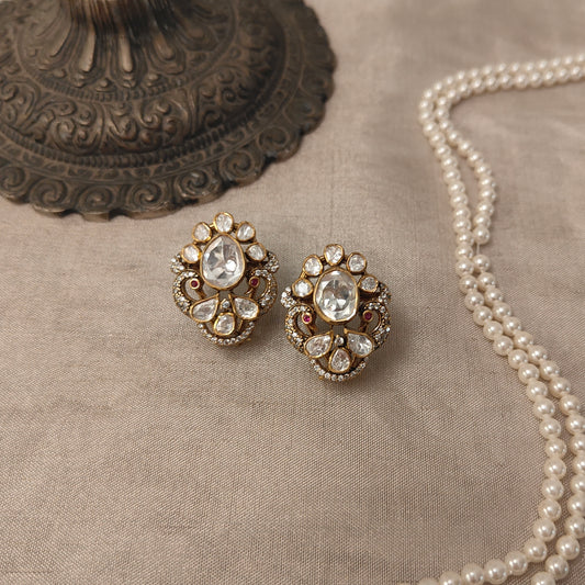 "Gold-plated polki  Noor Classic stud earrings with oval centerpiece and floral crystal design by Arka Jaipur", "Traditional kundan-style stud earrings with polki stones and ruby accents","Designer Indian stud earrings with floral motif and diamond-style detailing","Luxury heritage stud earrings handcrafted in Jaipur with polki and crystal work"