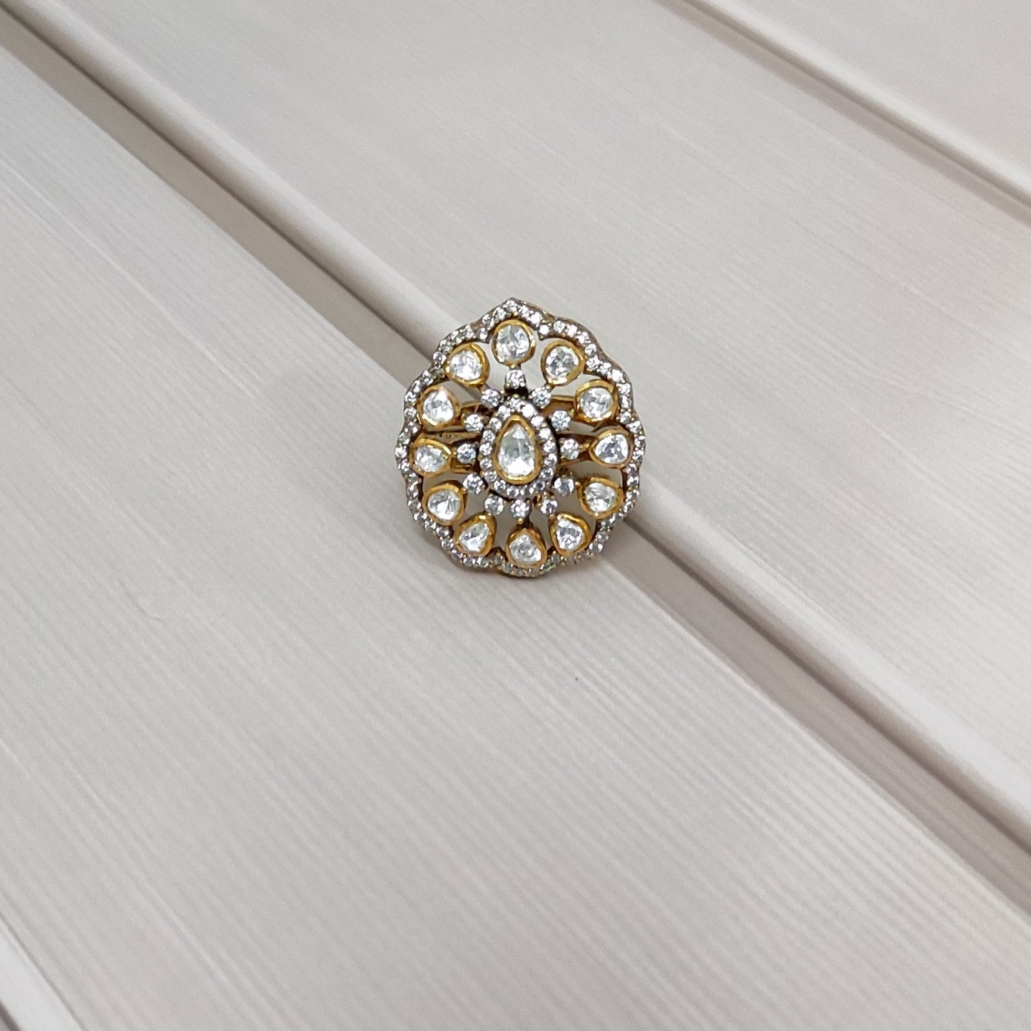“Polki Blossom Ring by Arka Jaipur with uncut Polki stones in a floral design, teardrop centre stone, kundan-style detailing, and crystal halo photographed on a beige textured background.”
