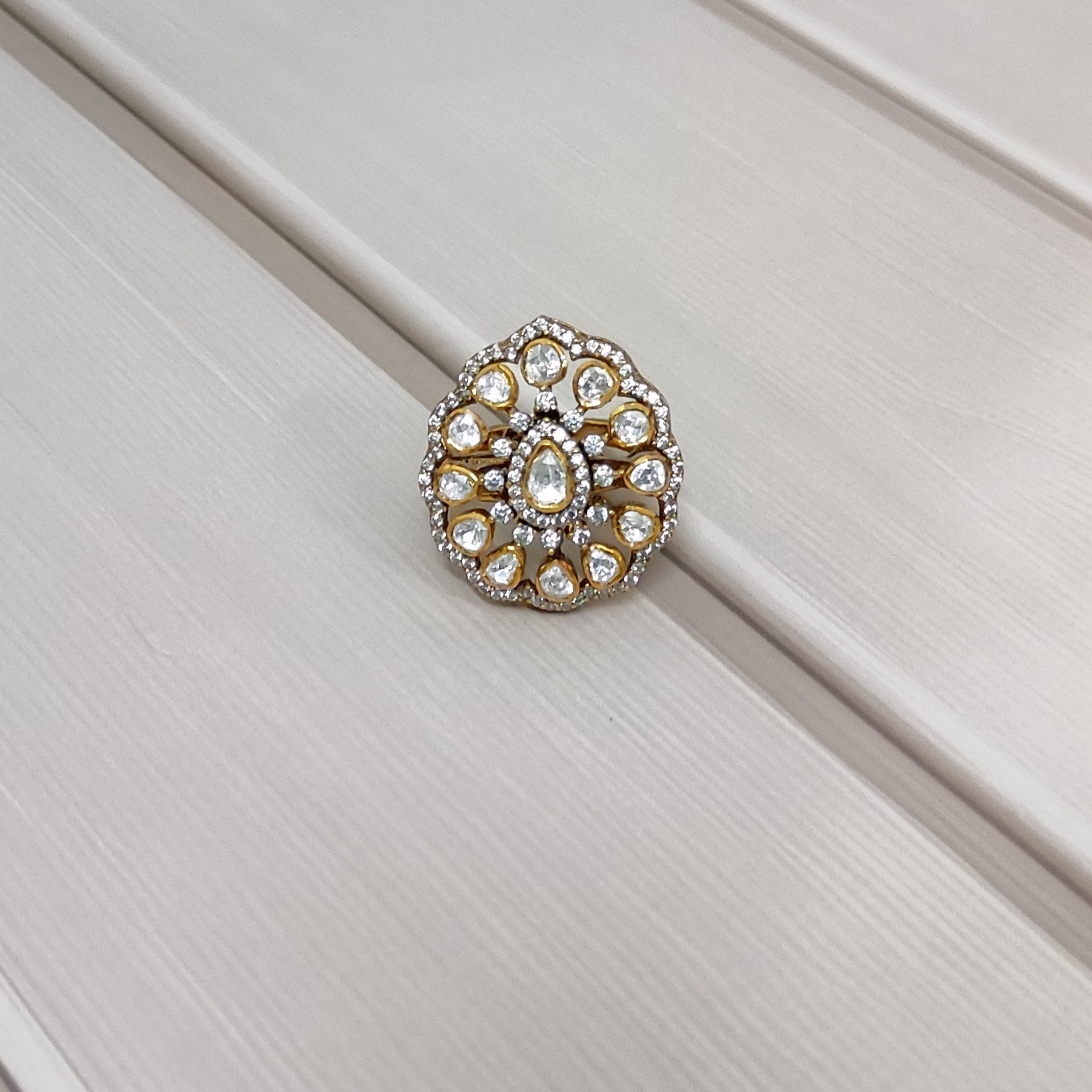 “Polki Blossom Ring by Arka Jaipur with uncut Polki stones in a floral design, teardrop centre stone, kundan-style detailing, and crystal halo photographed on a beige textured background.”