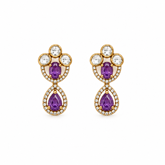 A pair of gold drop earrings featuring purple pear-cut center stones, surrounded by clear round and marquise-cut stones in gold settings, shown on a plain white background.