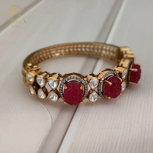 Celebrate royal artistry with the Ruby Majesty Bangle by Arka Jaipur. Handcrafted in gold-plated 925 silver, this exquisite design features carved ruby gemstones framed with uncut polki-style stones and delicate pavé detailing. A perfect heritage-inspired jewel that blends vibrant tradition with timeless elegance, ideal for weddings and festive occasions.