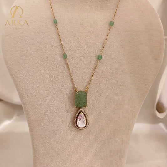 "Elysian Emerald Drop Pendant Handcrafted  by Arka Jaipur with carved green gemstone top and teardrop Polki stone drop, outlined with CZ stones, displayed on a wooden background"