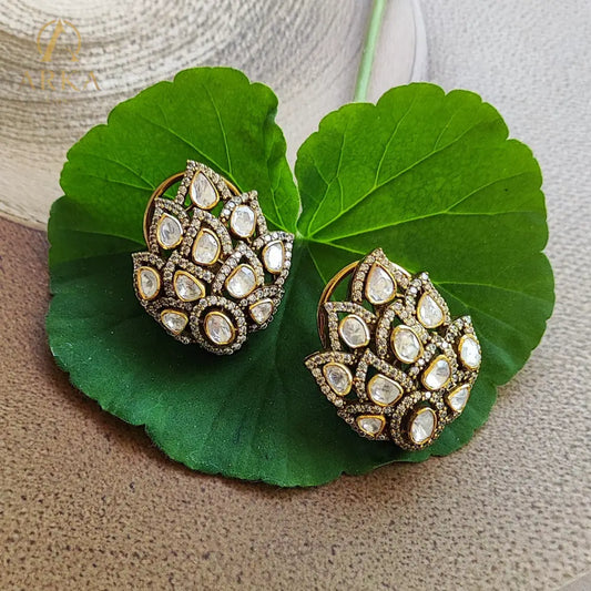 These exquisite Kamalika earrings showcase a stunning floral-inspired cluster design, crafted with teardrop-shaped stones arranged in a layered petal motif. Set in a rich gold-tone Sterling Silver base and bordered with delicate pavé crystals, the design radiates elegance and grandeur. Perfect for weddings, festive occasions, and evening celebrations, these statement studs add timeless charm and brilliance to any look.