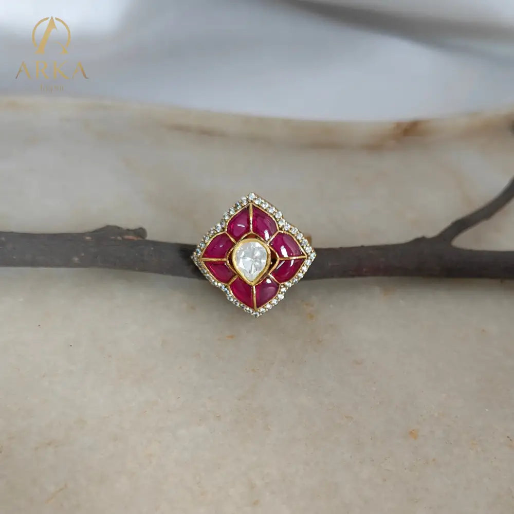 “Lotus Bloom Ring by Arka Jaipur with ruby enamel petals and central polki-style stone displayed on a natural twig over a marble background.”