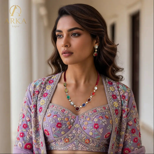 "Model wearing Navratna Radiance Set kundan necklace set by Arka Jaipur with nine colorful gemstones and matching earrings, styled with a floral embroidered lilac lehenga – traditional Indian jewelry"
