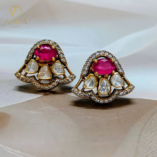 “Scarlet Mist earrings by Arka Jaipur – modern chic designer stud earrings with oval ruby centerpiece, teardrop white stones, gold finish, and diamond outline.”