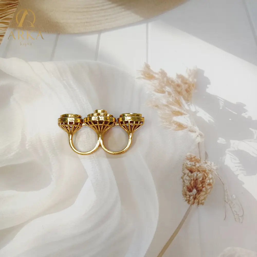 “Back view of the Twin Bloom Ring by Arka Jaipur showing the gold dual-finger ring structure and intricate raised floral stone settings, placed on a textured beige fabric background.”